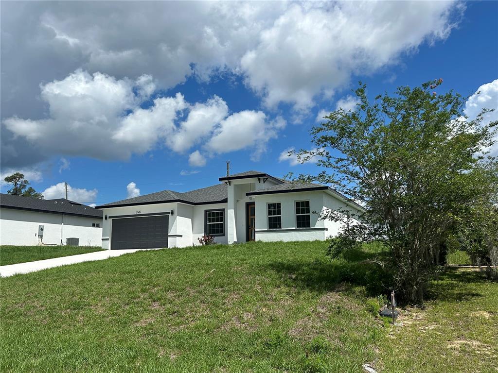 A modern, single-story white house with a dark garage door and a sloped grassy lawn — 17145 SW 44TH CIRCLE, OCALA, FL