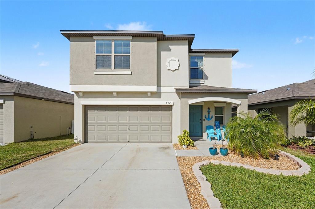 A two-story house with a beige stucco exterior, a two-car garage, and a front porch — 882 OLIVE CONCH STREET, RUSKIN, FL