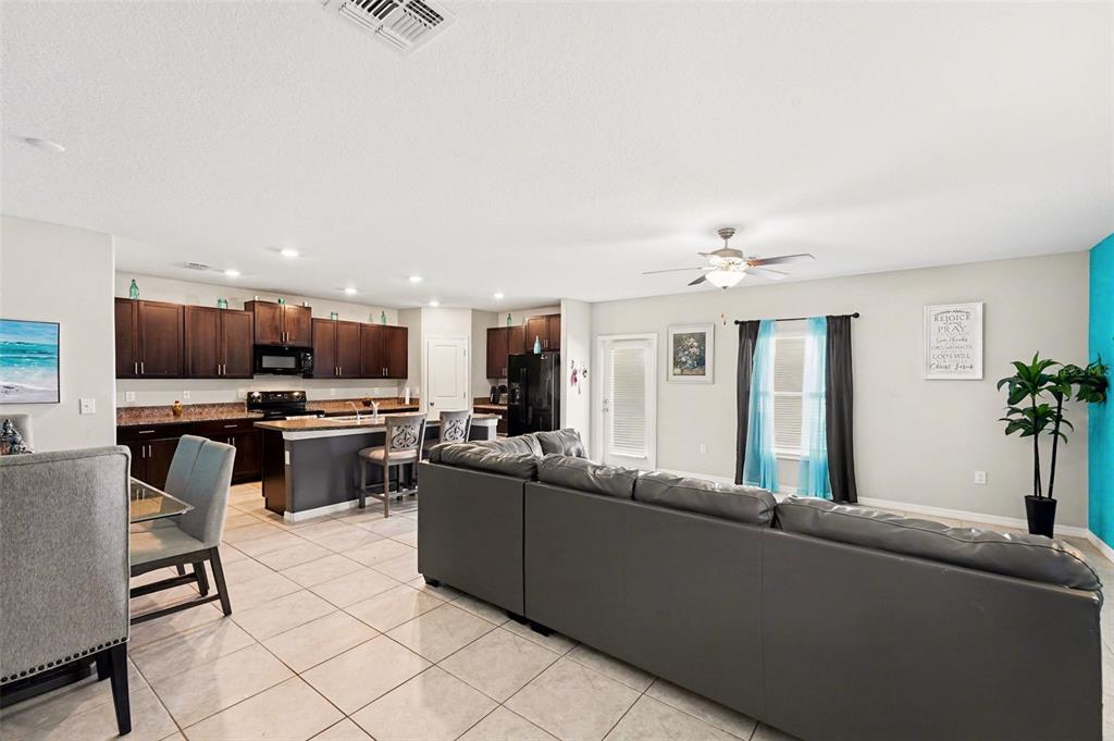 An open-concept living room and kitchen featuring dark cabinetry, tile flooring, and a gray sofa — 882 OLIVE CONCH STREET, RUSKIN, FL