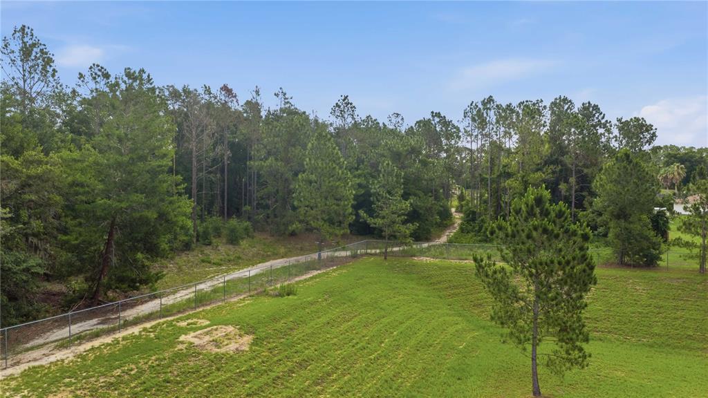 An aerial view shows a grassy lot bordered by a chain-link fence and dense woods — TBD CR-25, BELLEVIEW, FL