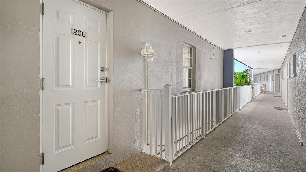 A white door labeled 200 opens onto an outdoor apartment building walkway with metal railings — 3453 GULF OF MEXICO DRIVE UNIT 200, LONGBOAT KEY, FL