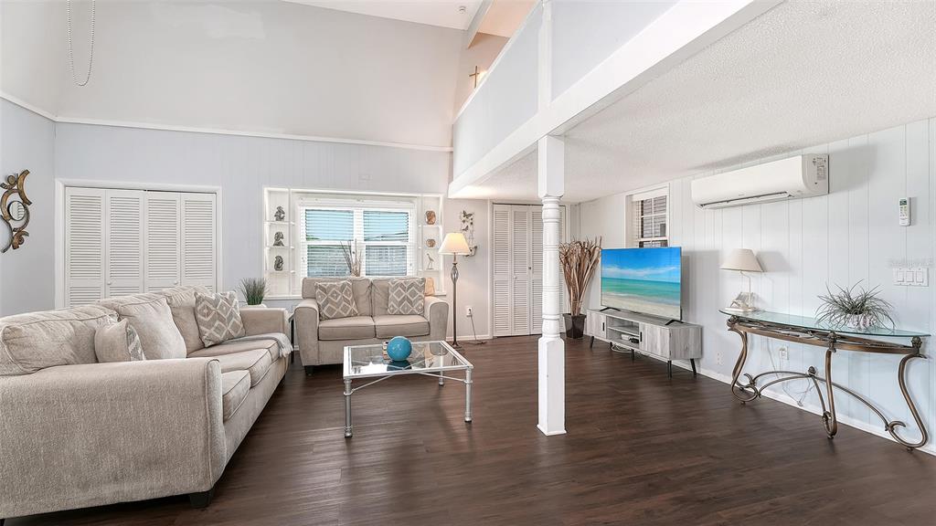 A living room with vaulted ceilings, a loft area, wood-look flooring, and a wall-mounted air conditioner — 3453 GULF OF MEXICO DRIVE UNIT 200, LONGBOAT KEY, FL