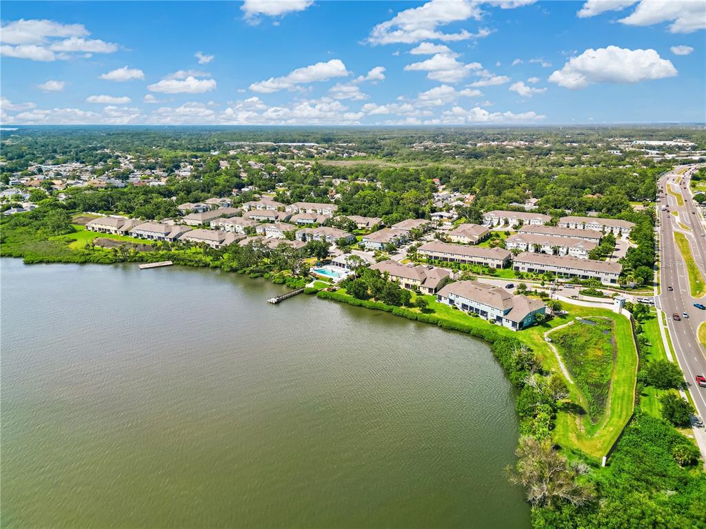 An aerial view shows a lakeside apartment complex with a pool and adjacent highway — 1309 SUNSET WIND LOOP, OLDSMAR, FL
