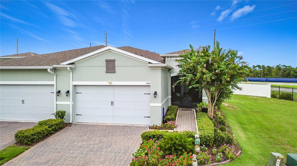 An exterior view of a light green house with a two-car garage and landscaped yard — 1987 KEY BAY TRAIL, KISSIMMEE, FL