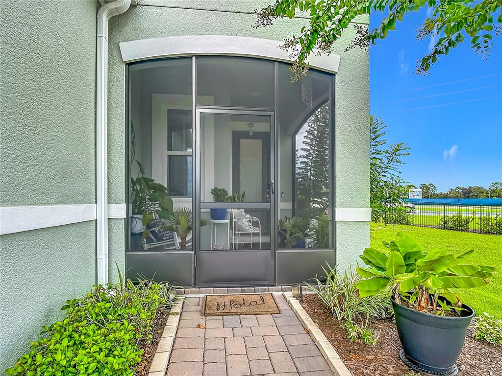 A paved walkway leads to a screened-in front porch with a door and potted plants — 1987 KEY BAY TRAIL, KISSIMMEE, FL