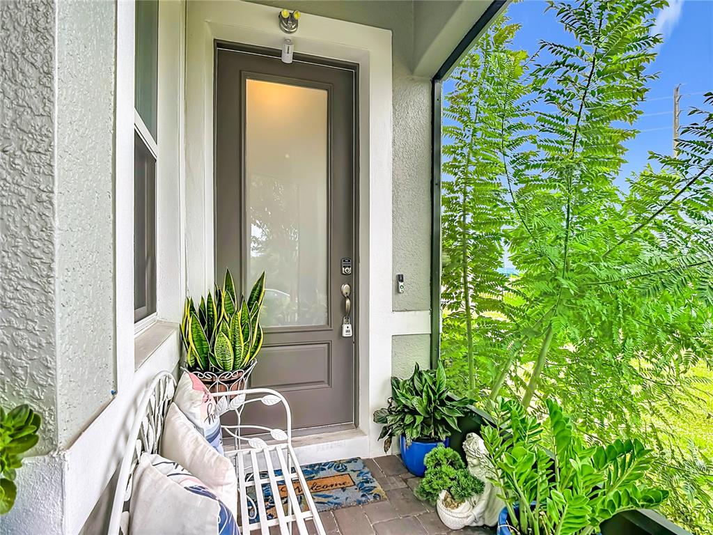 A covered front porch features a gray door, a white metal bench, and potted plants — 1987 KEY BAY TRAIL, KISSIMMEE, FL