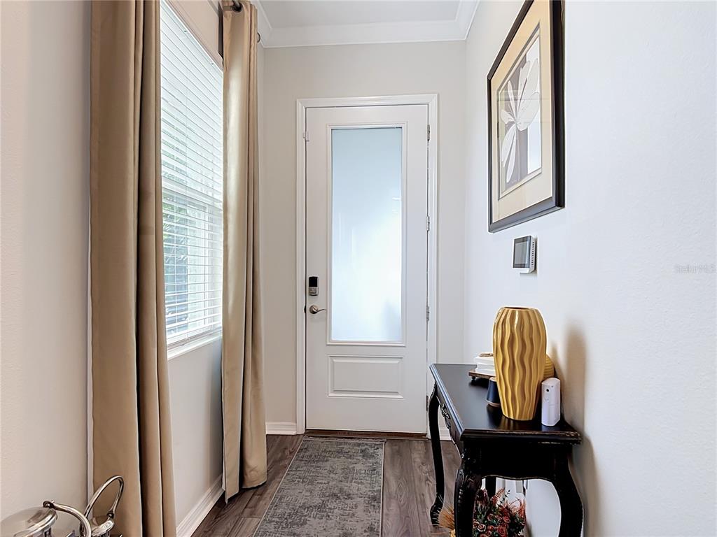 A bright entryway features a white door with frosted glass, wood flooring, and a console table — 1987 KEY BAY TRAIL, KISSIMMEE, FL