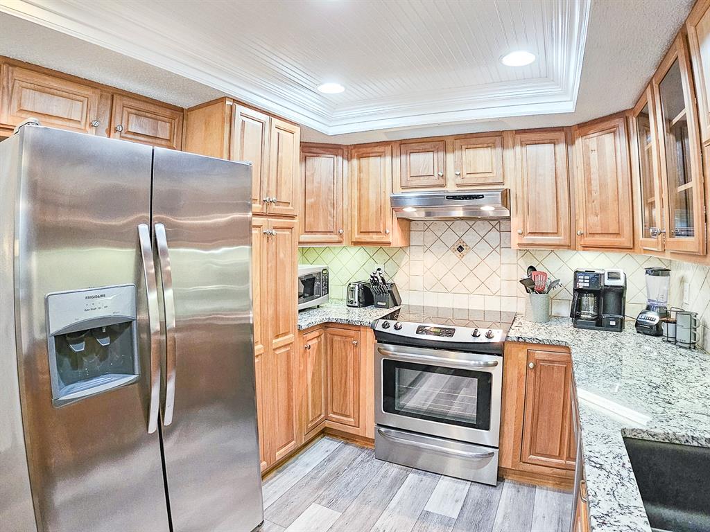 A kitchen features stainless steel appliances, wood cabinets, granite countertops, and light-colored wood flooring — 2 DONDANVILLE ROAD UNIT 112, ST AUGUSTINE, FL