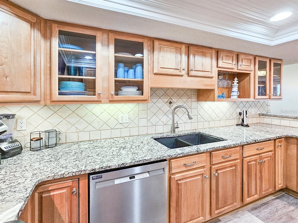 A kitchen features light wood cabinets, granite countertops, a stainless dishwasher, and a tiled backsplash — 2 DONDANVILLE ROAD UNIT 112, ST AUGUSTINE, FL