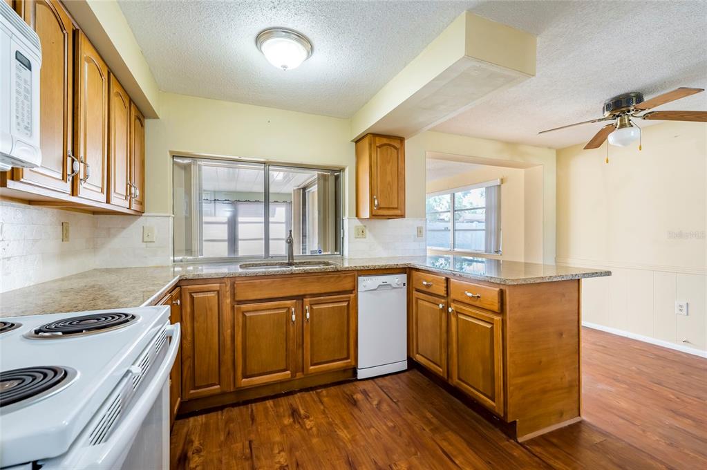 A kitchen with wooden cabinets, granite countertops, a white dishwasher, and wood-look flooring — 3246 BROOKFIELD DRIVE, HOLIDAY, FL