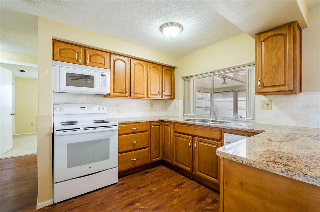 A kitchen with wood cabinets, granite countertops, white appliances, and wood-look flooring — 3246 BROOKFIELD DRIVE, HOLIDAY, FL