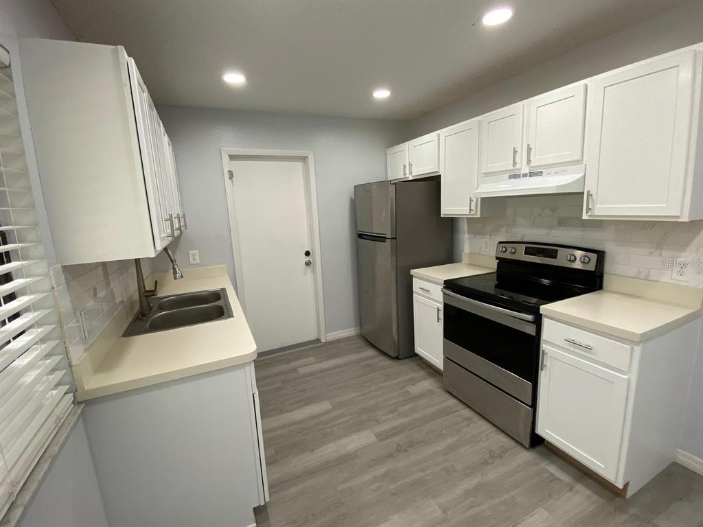 A kitchen features white cabinets, stainless steel appliances, light countertops, and gray wood-look flooring — 5 HICKORY TRACK RUN, OCALA, FL
