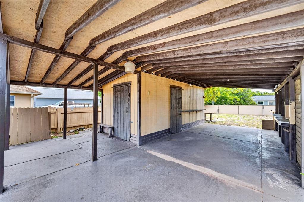 A covered concrete carport features two wooden storage sheds and an outdoor sink area — 1961 CAROLINA AVENUE, ORMOND BEACH, FL