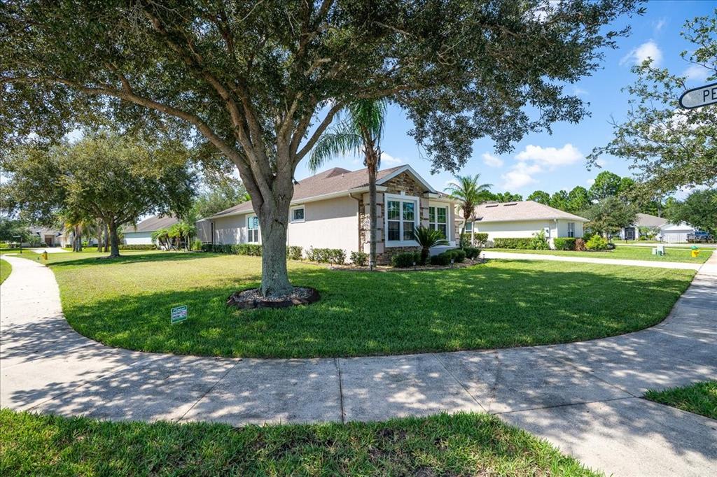 A single-story house with a stone facade sits on a corner lot with large trees — 101 MCGILL CIRCLE, DAYTONA BEACH, FL