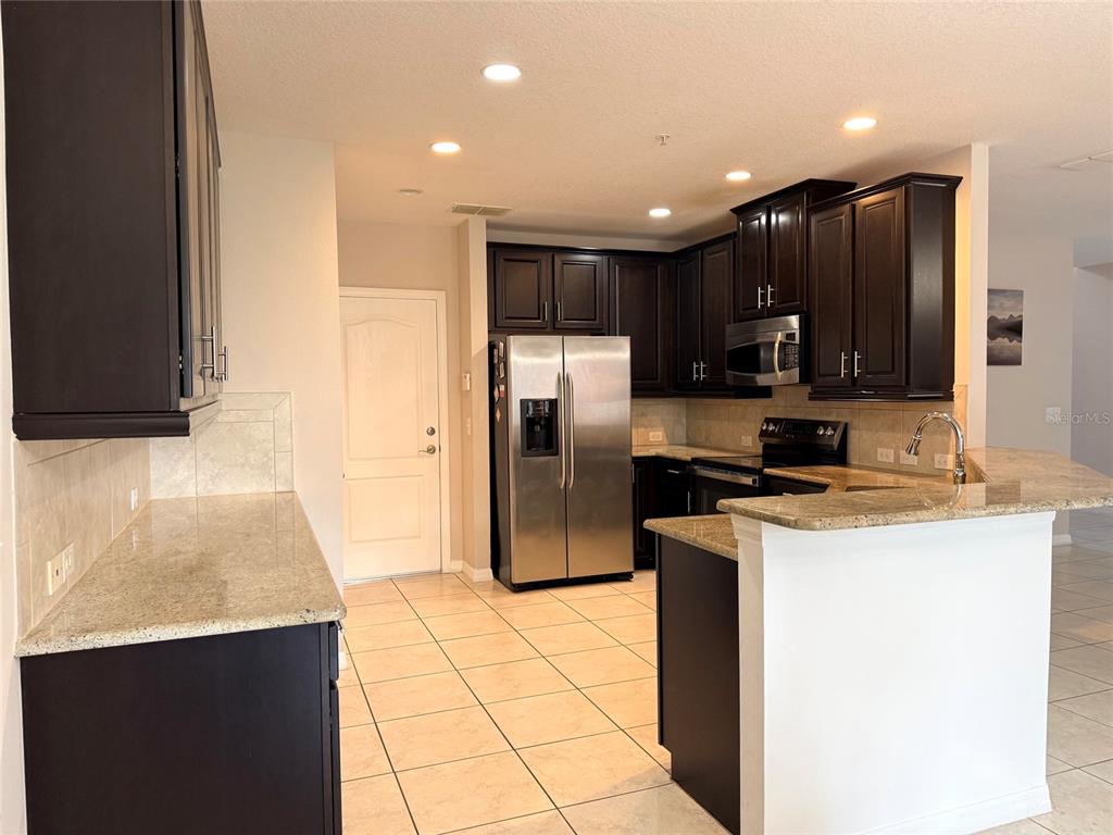 A kitchen features dark wood cabinets, granite countertops, stainless steel appliances, and tile flooring — 2084 WATER TUPELO WAY, OCOEE, FL