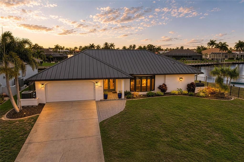 A single-story house with a dark metal roof and a concrete driveway sits waterfront — 602 VIA TUNIS, PUNTA GORDA, FL