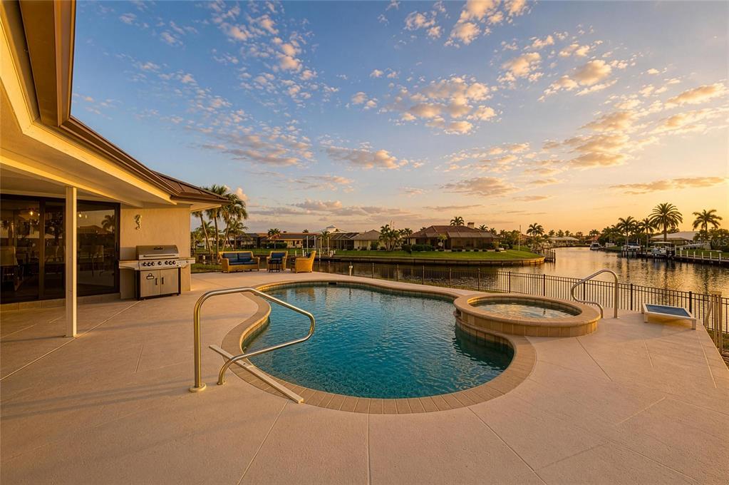 A patio with a swimming pool and spa overlooks a canal at sunset — 602 VIA TUNIS, PUNTA GORDA, FL