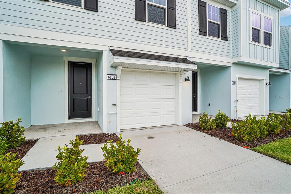 A light blue two-story townhouse exterior features a black front door and a white garage — 6868 HOLCOMBE DOWN DRIVE, ZEPHYRHILLS, FL