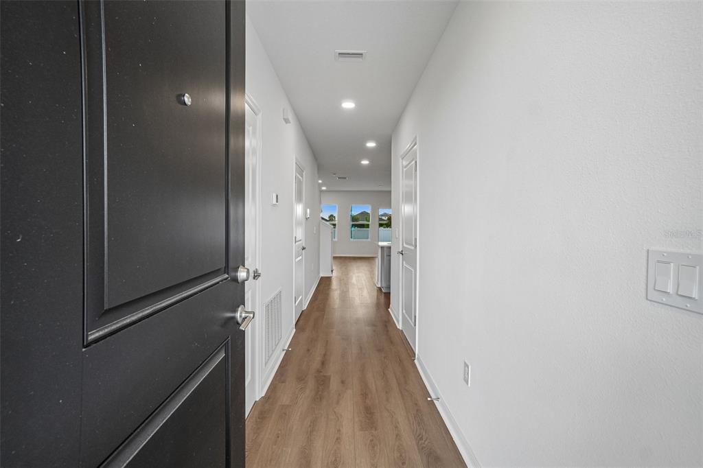 A view from an open doorway looking down a hallway with wood-look flooring — 6868 HOLCOMBE DOWN DRIVE, ZEPHYRHILLS, FL