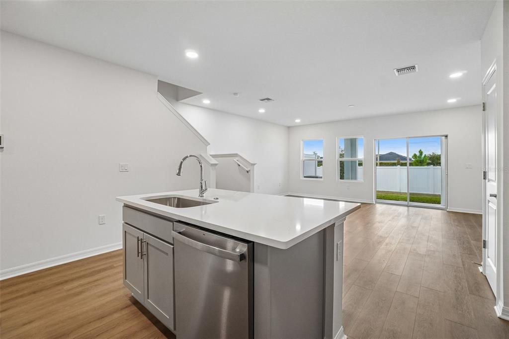 A kitchen island with a stainless steel dishwasher and sink faces an open living area — 6868 HOLCOMBE DOWN DRIVE, ZEPHYRHILLS, FL