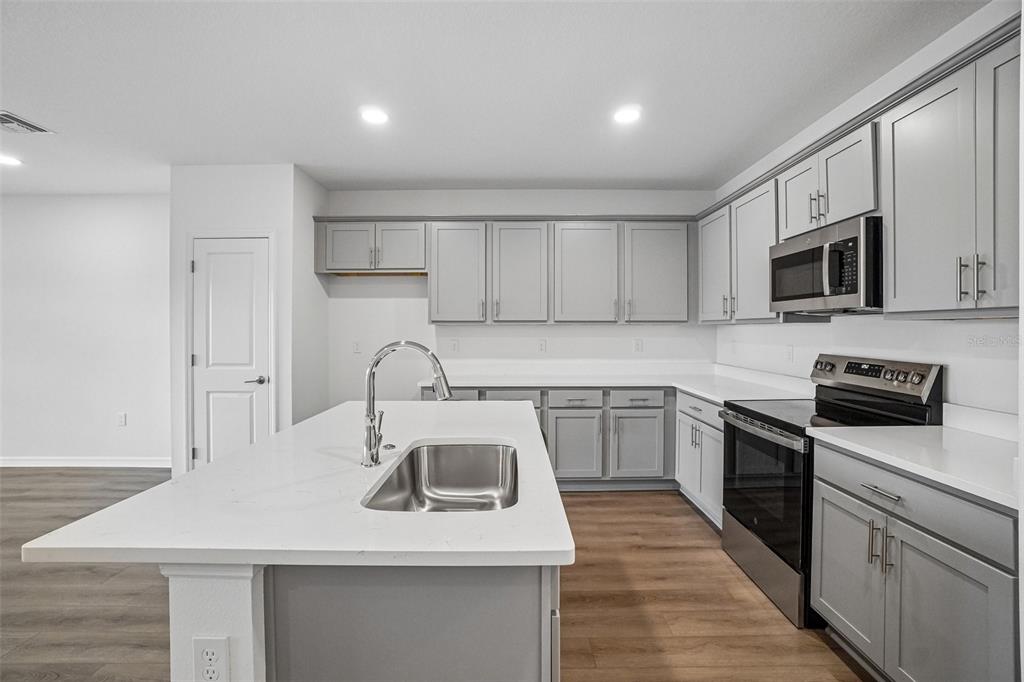 A modern kitchen features gray cabinets, white countertops, a center island, and stainless steel appliances — 6868 HOLCOMBE DOWN DRIVE, ZEPHYRHILLS, FL