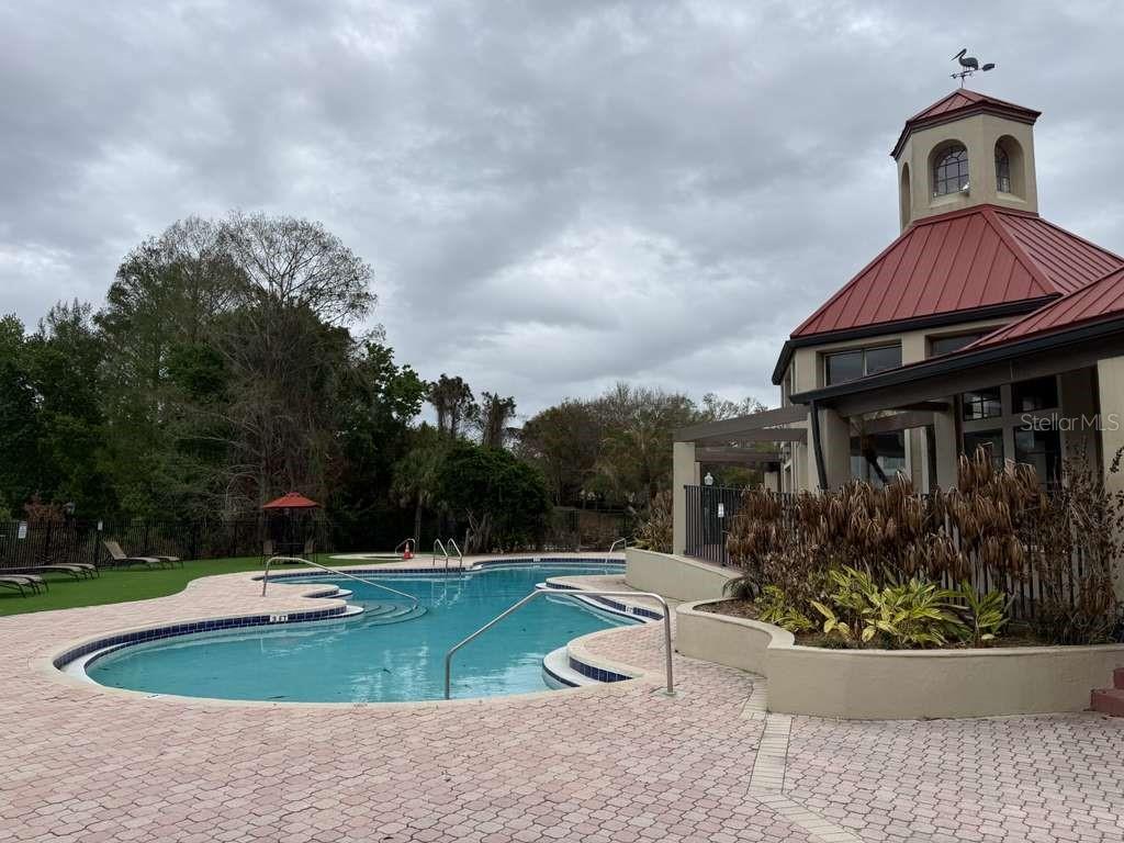 A swimming pool with a paved deck sits beside a building with a red roof — 216 AFTON SQUARE UNIT 304, ALTAMONTE SPRINGS, FL