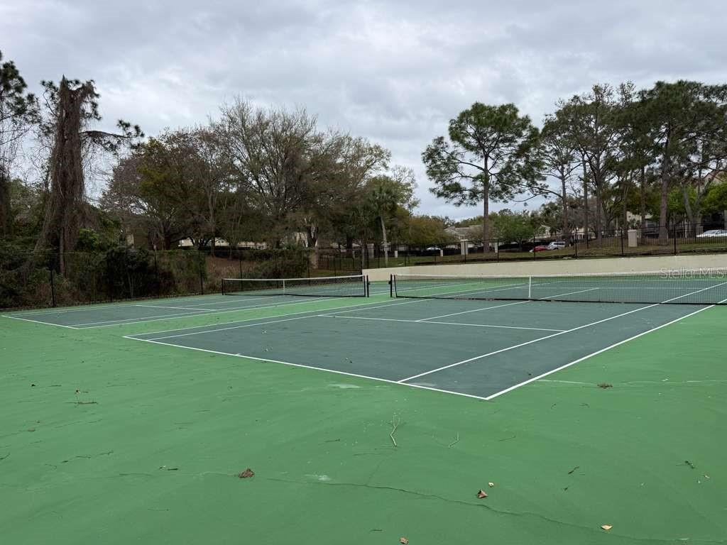 Two outdoor tennis courts with green surfaces and nets are surrounded by trees and fencing — 216 AFTON SQUARE UNIT 304, ALTAMONTE SPRINGS, FL