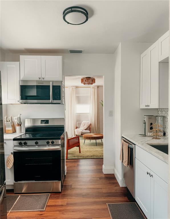 A kitchen with white cabinets and stainless steel appliances leads into a living area — 107 4TH AVENUE, ST PETE BEACH, FL
