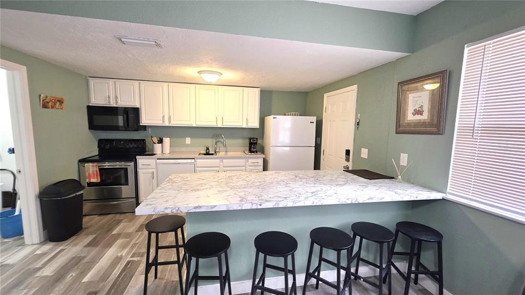 A kitchen with white cabinets, stainless steel appliances, and a marble-patterned breakfast bar with stools — 2031 4TH STREET, SARASOTA, FL