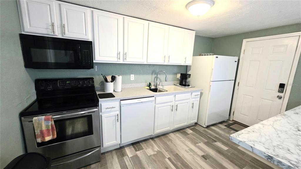 A kitchen features white cabinets, stainless steel appliances, a white refrigerator, and gray wood-look flooring — 2031 4TH STREET, SARASOTA, FL
