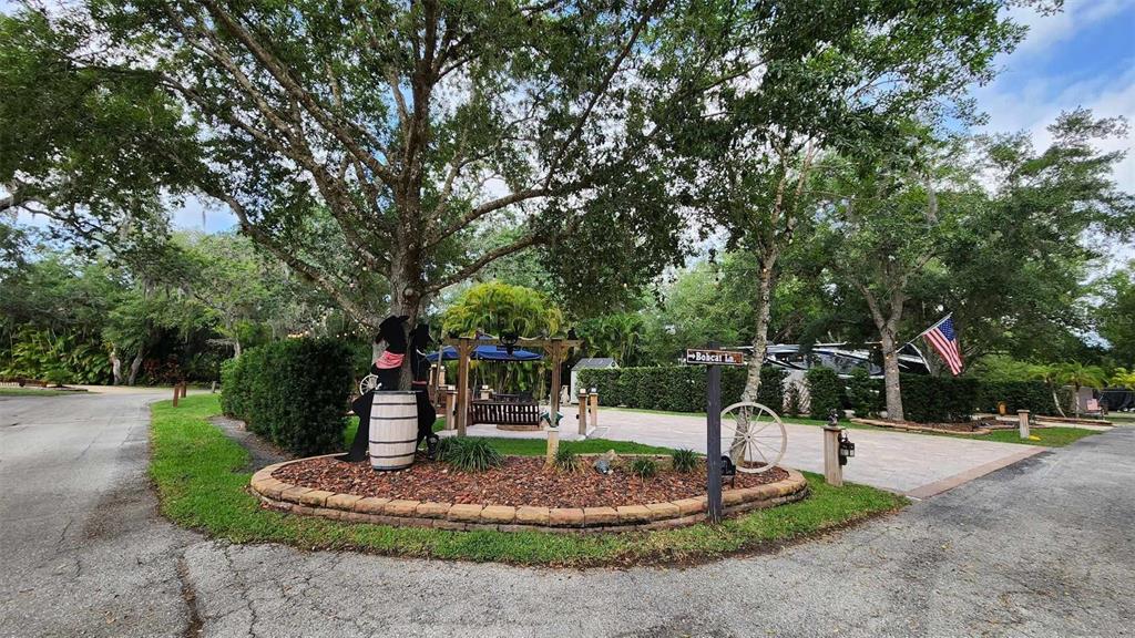 A landscaped island with a wooden barrel and a street sign sits before a paved driveway — 371 BOB CAT LANE, RIVER RANCH, FL