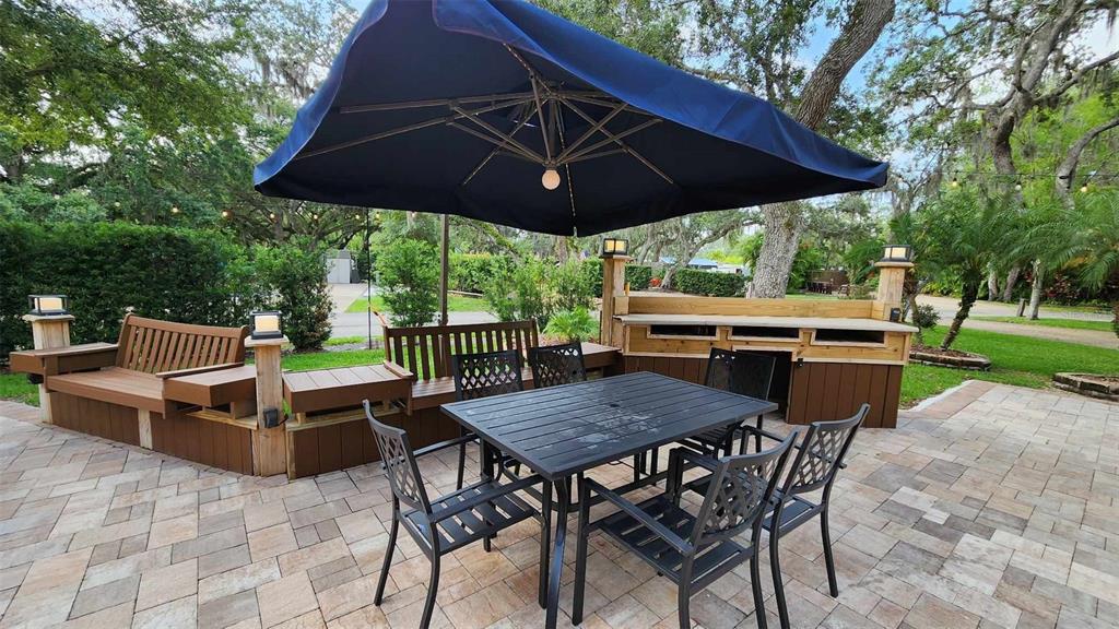 A paved outdoor patio features a dining set, a large umbrella, and built-in wooden seating — 371 BOB CAT LANE, RIVER RANCH, FL
