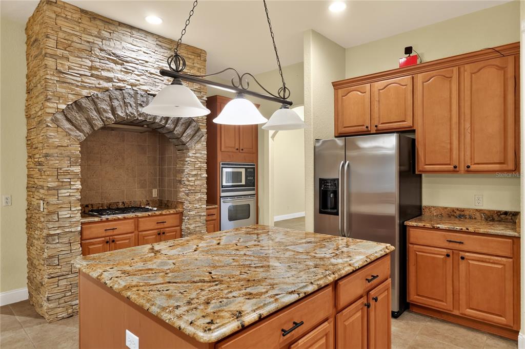A kitchen features a stone-encased stove alcove, granite countertops, wood cabinets, and a central island — 3049 W LAUREL STREET, LECANTO, FL