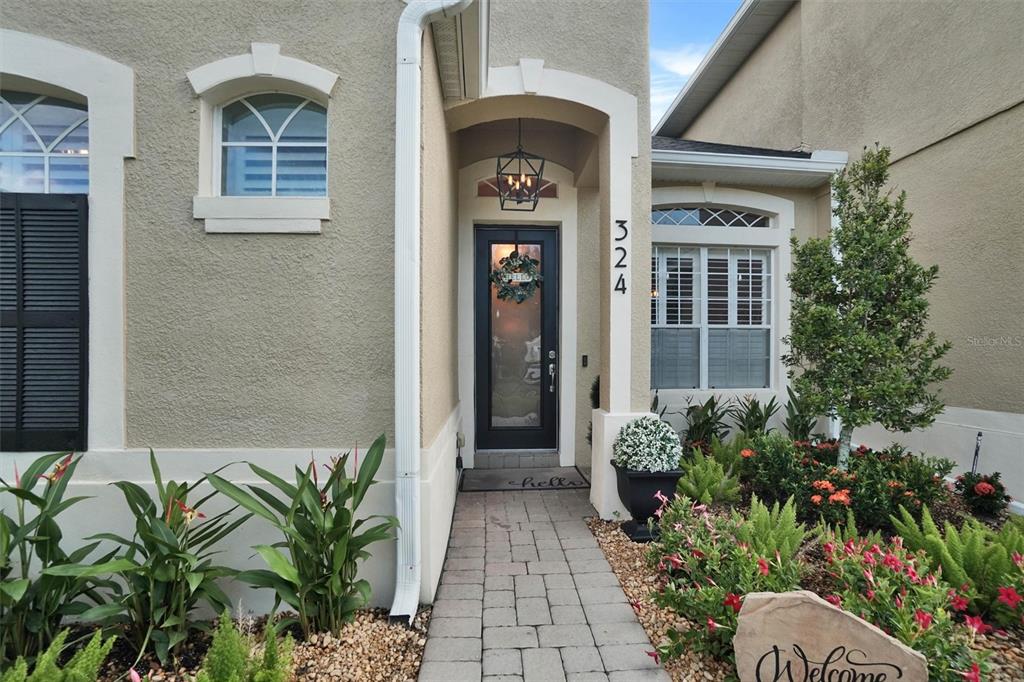 A paved walkway leads to the front entrance of a beige stucco house with landscaping — 324 TUDOR SPRING COURT, ORLANDO, FL