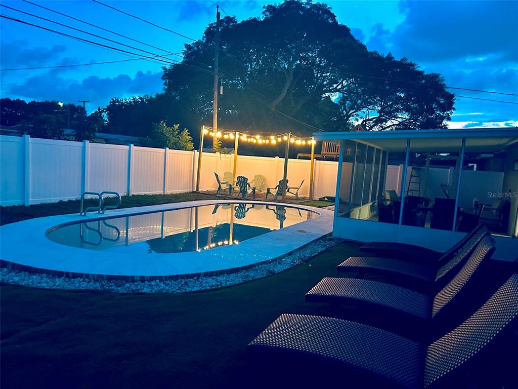 A backyard swimming pool with lounge chairs and string lights at dusk — 1443 JEFFORDS ST, CLEARWATER, FL