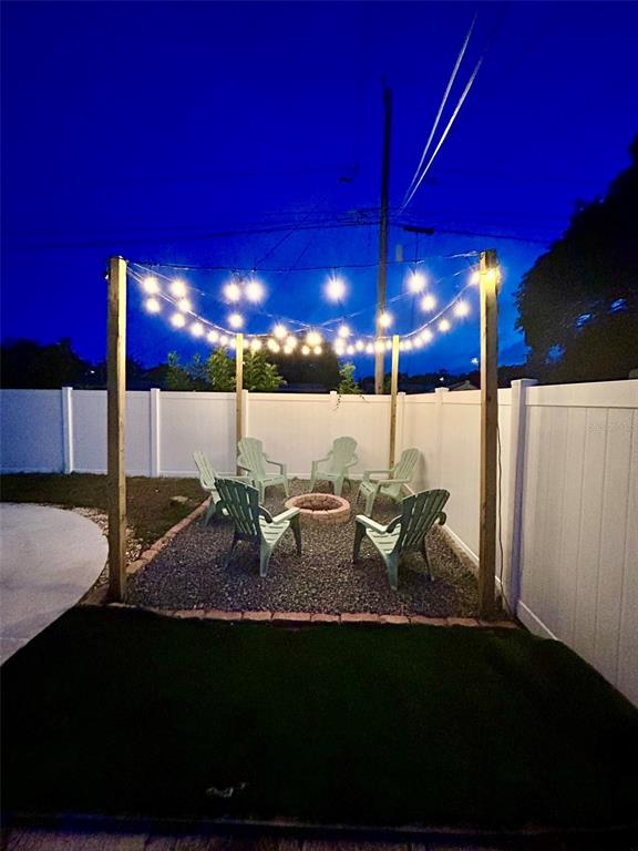 A backyard fire pit area features gravel flooring, Adirondack chairs, and overhead string lights — 1443 JEFFORDS ST, CLEARWATER, FL