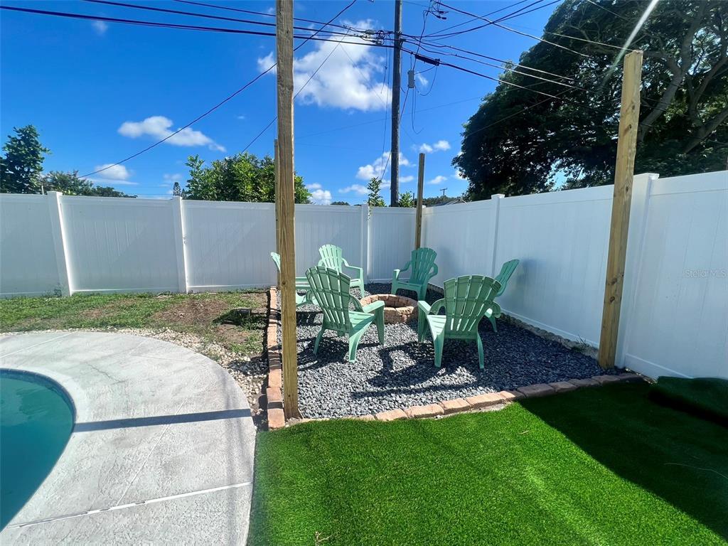 A backyard fire pit area features four green Adirondack chairs on gravel near a pool — 1443 JEFFORDS ST, CLEARWATER, FL