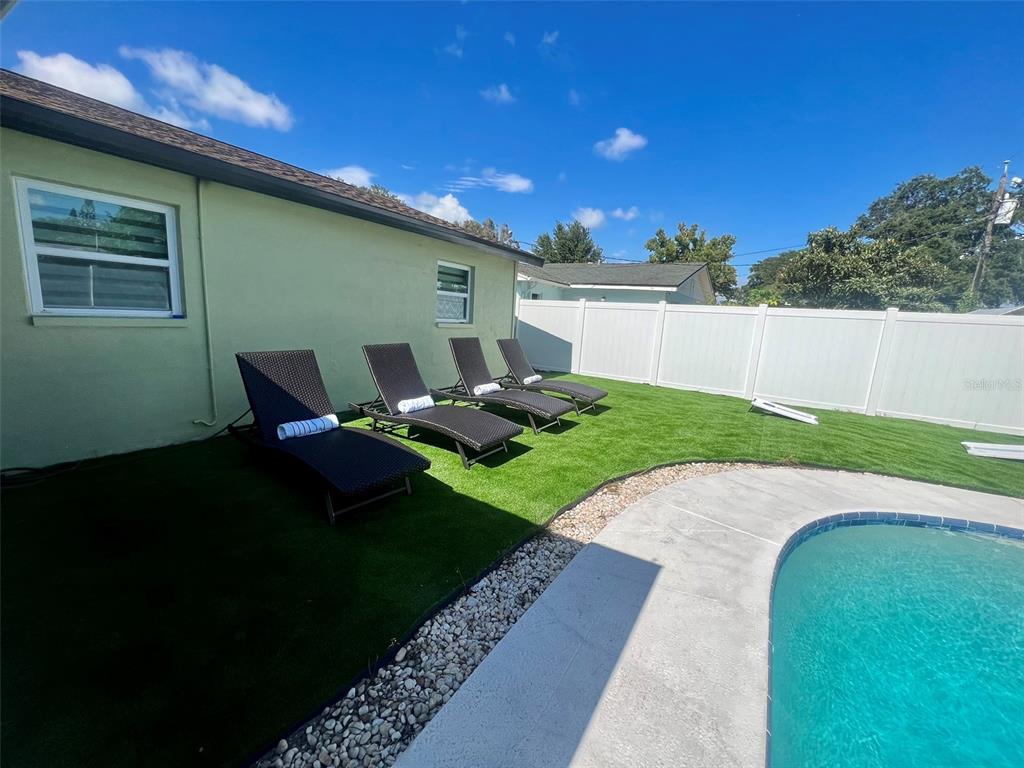 Four lounge chairs sit on artificial turf beside a swimming pool and white privacy fence — 1443 JEFFORDS ST, CLEARWATER, FL