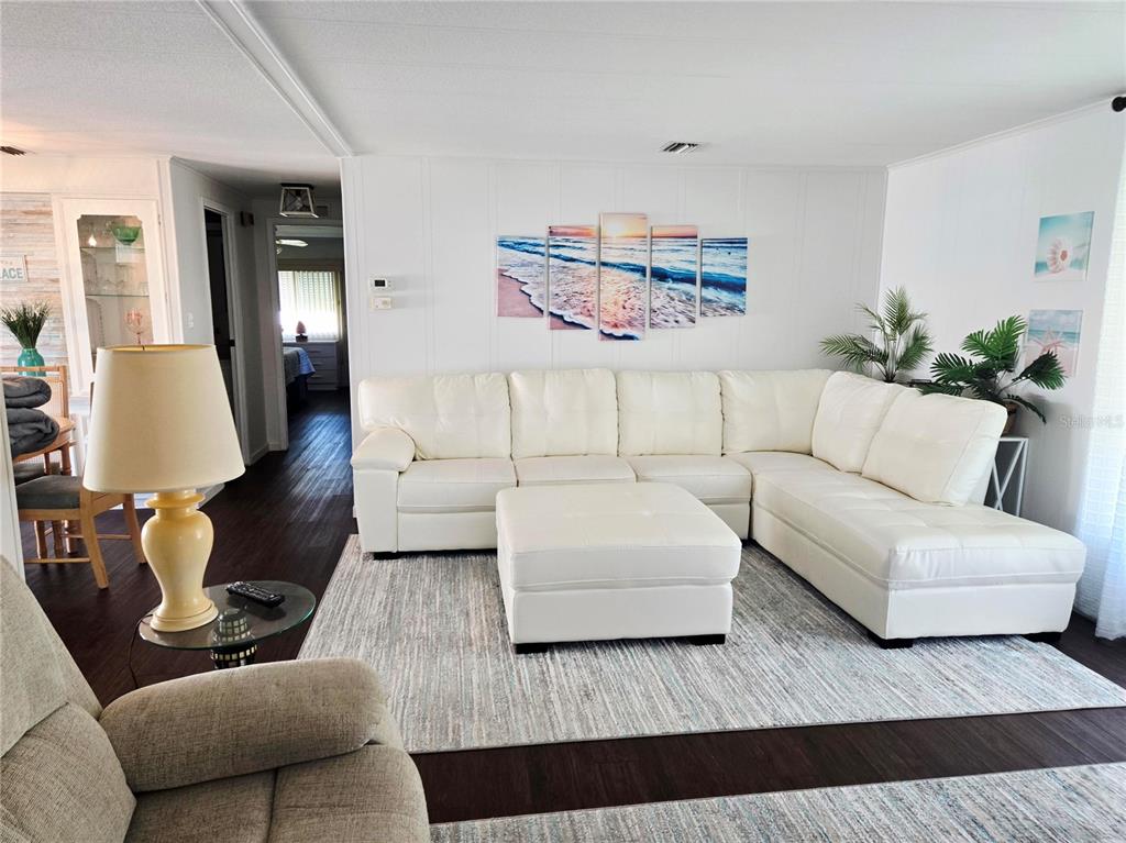 A living room features a white sectional sofa, a matching ottoman, and a beach-themed wall art — 5316 53RD AVE E UNIT D14, BRADENTON, FL