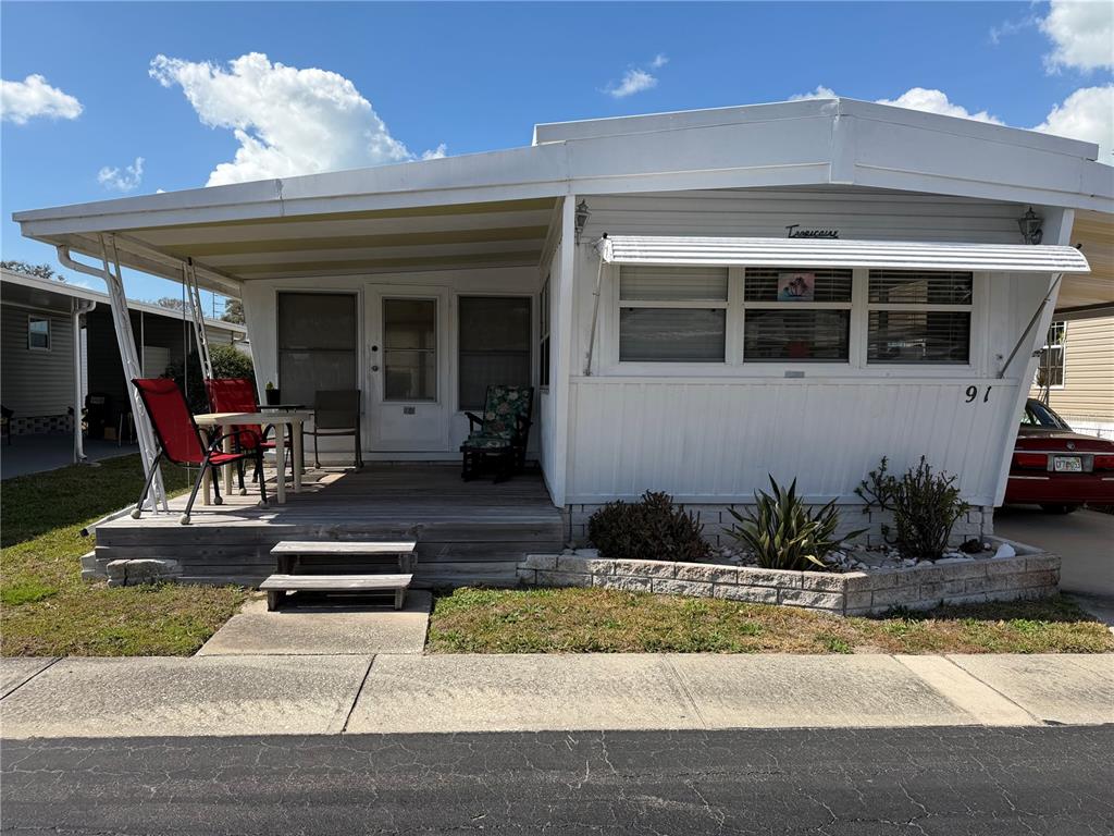 A single-story mobile home features a white exterior, a wooden front porch, and a carport — 1040 MAIN STREET UNIT 91, DUNEDIN, FL
