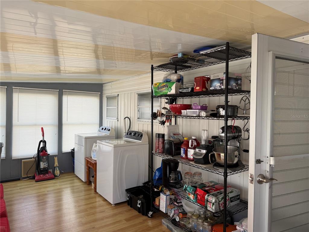 A laundry room features a white washer and dryer, a metal shelving unit, and wood-look flooring — 1040 MAIN STREET UNIT 91, DUNEDIN, FL
