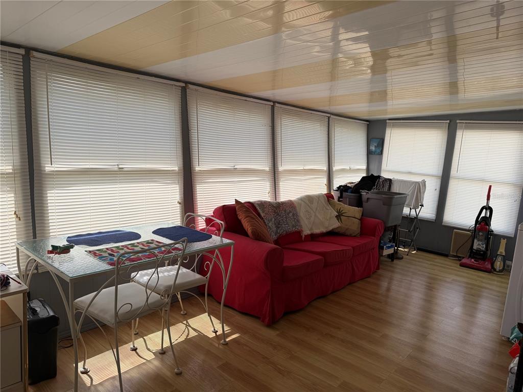 A sunroom features a red sofa, a glass dining table, and light wood-look flooring — 1040 MAIN STREET UNIT 91, DUNEDIN, FL