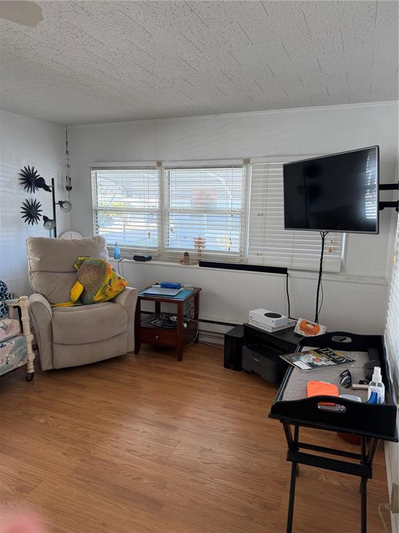 A living room features wood-look flooring, a recliner, a wall-mounted television, and window blinds — 1040 MAIN STREET UNIT 91, DUNEDIN, FL