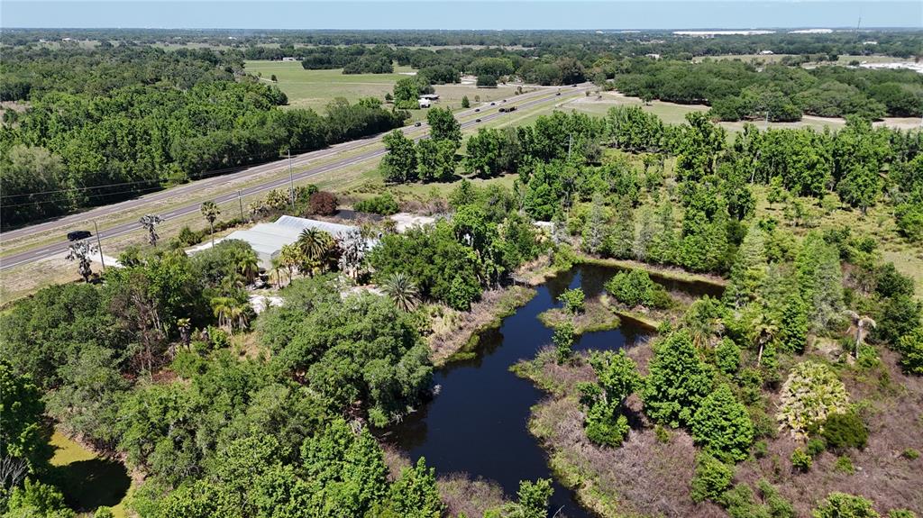An aerial view shows a building surrounded by trees and a pond near a highway — 6501 STATE ROAD 60 E, BARTOW, FL