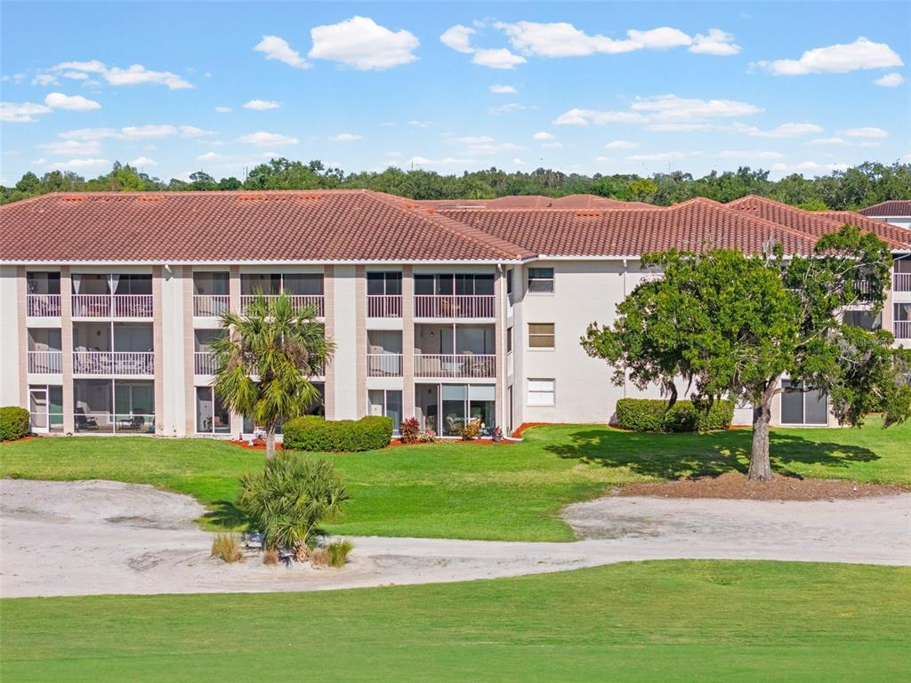 A multi-story apartment building with screened balconies overlooks a grassy golf course — 6503 STONE RIVER ROAD UNIT 204, BRADENTON, FL