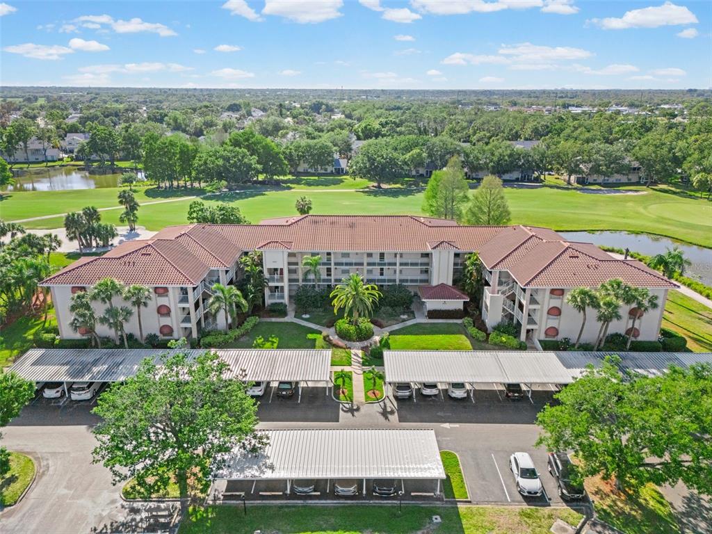An aerial view of a multi-story apartment building with covered parking and a golf course — 6503 STONE RIVER ROAD UNIT 204, BRADENTON, FL