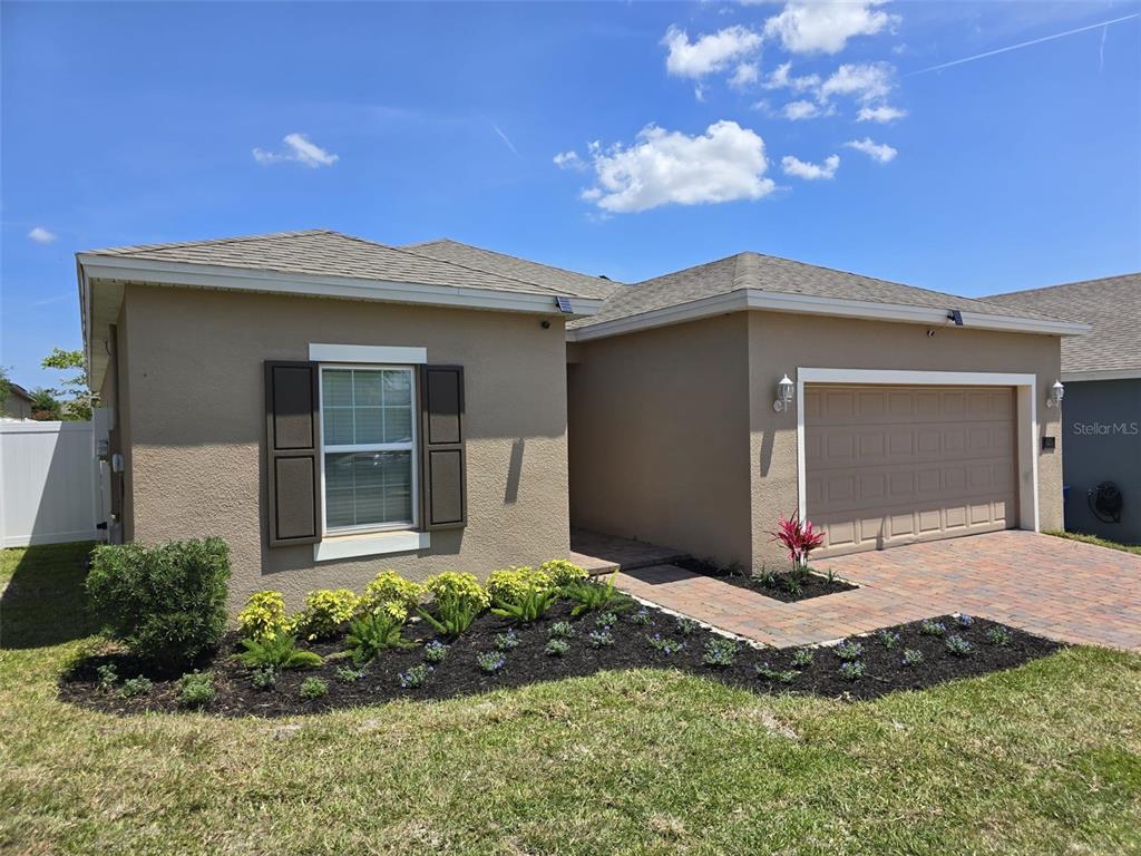 A single-story house with a tan stucco exterior, a two-car garage, and a landscaped yard — 625 DISA DRIVE, DAVENPORT, FL