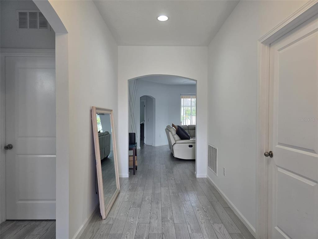 A hallway with light wood-look flooring leads through an arched doorway into a living area — 625 DISA DRIVE, DAVENPORT, FL