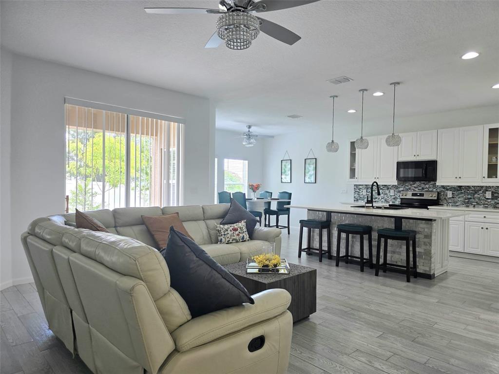 An open-concept living room and kitchen feature white cabinetry, a stone-tiled island, and gray flooring — 625 DISA DRIVE, DAVENPORT, FL