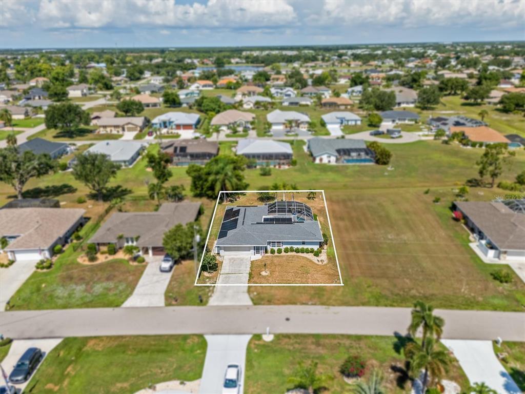 An aerial view shows a single-story house with a pool cage and solar panels — 26392 LANCER LANE, PUNTA GORDA, FL